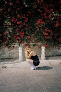 a woman crouching down in front of red flowers